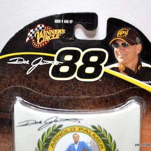 May include: A die-cast car package featuring a portrait of a man wearing a UPS hat and sunglasses. The package has the number "88" in large white letters, the words "Winners Circle", and the signature "Dale Jarrett". The package is brown, black, and yellow.