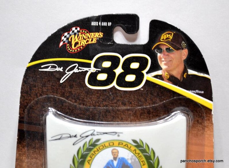 May include: A die-cast car package featuring a portrait of a man wearing a UPS hat and sunglasses. The package has the number "88" in large white letters, the words "Winners Circle", and the signature "Dale Jarrett". The package is brown, black, and yellow.