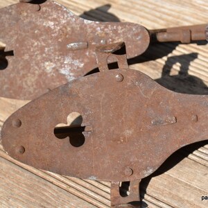May include: Two antique metal ice skates with a heavy rusted patina. Each skate features a pointed toe plate with a clover-shaped cutout, metal rivets, and an adjustable heel mechanism. The text panchosporch.etsy.com is visible in the corner.