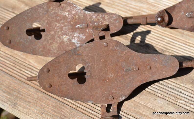 May include: Two antique metal ice skates with a heavy rusted patina. Each skate features a pointed toe plate with a clover-shaped cutout, metal rivets, and an adjustable heel mechanism. The text panchosporch.etsy.com is visible in the corner.