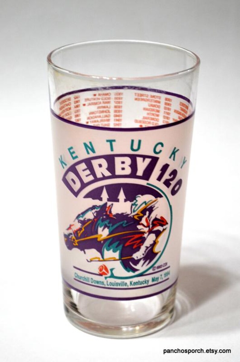Puede incluir: Vaso de vidrio transparente con el logotipo de Kentucky Derby 120, que muestra una escena de carreras de caballos en morado, turquesa y rojo. El vaso incluye el texto "Churchill Downs, Louisville, Kentucky May 7, 1994".