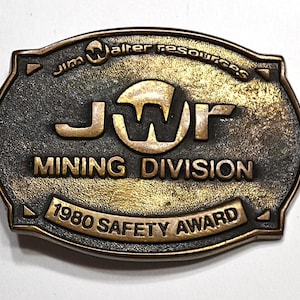 May include: Vintage bronze-toned metal Mining Division award. The oval-shaped award features the text "Jim Walter Resources," "JWR MINING DIVISION," and "1980 SAFETY AWARD." The metal has a textured, aged appearance.
