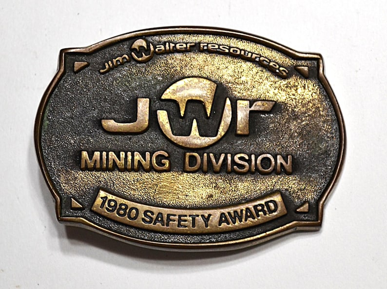 May include: Vintage bronze-toned metal Mining Division award. The oval-shaped award features the text "Jim Walter Resources," "JWR MINING DIVISION," and "1980 SAFETY AWARD." The metal has a textured, aged appearance.