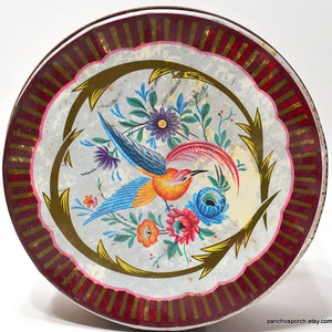 May include: A vintage round tin with a red and gold border. The center features a colorful bird with a long tail surrounded by flowers and leaves.