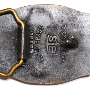 May include: Vintage solid brass belt buckle with a rectangular frame and an oval body. The buckle is marked "BIS SOLID BRASS" and "MADE IN U.S.A.". The metal has a tarnished, aged appearance.
