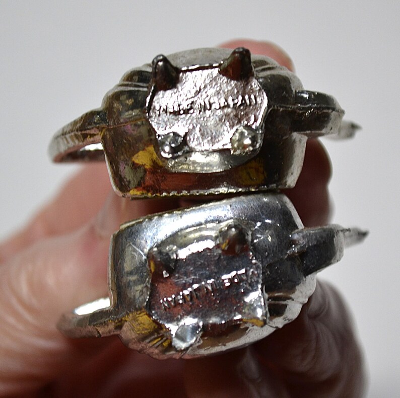 May include: Two silver-colored rings with a unique design. Each ring has a rectangular face with the text "MADE IN JAPAN". The rings have a textured surface and are stacked on top of each other.