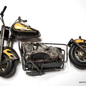 May include: A metal motorcycle sculpture with a black and yellow flame design on the gas tank and fenders. The sculpture has a detailed engine and wheels, and is made of metal.