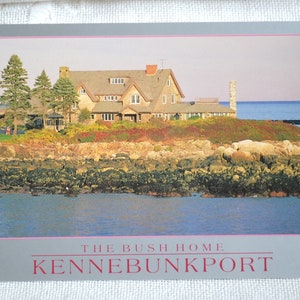 K&ouml;nnte beinhalten: Eine Postkarte mit einem Foto eines gro&szlig;en, hellbraunen Hauses mit einem grauen Dach. Das Haus liegt an einer felsigen K&uuml;ste mit Blick auf das Meer. Der Text "THE BUSH HOME KENNEBUNKPORT" ist auf der Postkarte gedruckt.