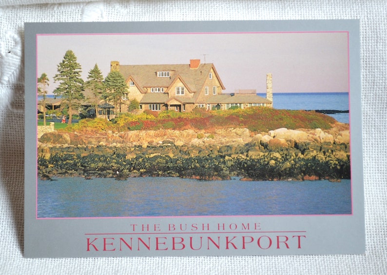 K&ouml;nnte beinhalten: Eine Postkarte mit einem Foto eines gro&szlig;en, hellbraunen Hauses mit einem grauen Dach. Das Haus liegt an einer felsigen K&uuml;ste mit Blick auf das Meer. Der Text "THE BUSH HOME KENNEBUNKPORT" ist auf der Postkarte gedruckt.