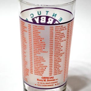 Puede incluir: Vaso transparente con una lista de ganadores de la Triple Corona de 1908 a 1961. El texto es rojo y blanco, con "Kentucky Derby" en morado. El vaso es cil&iacute;ndrico.