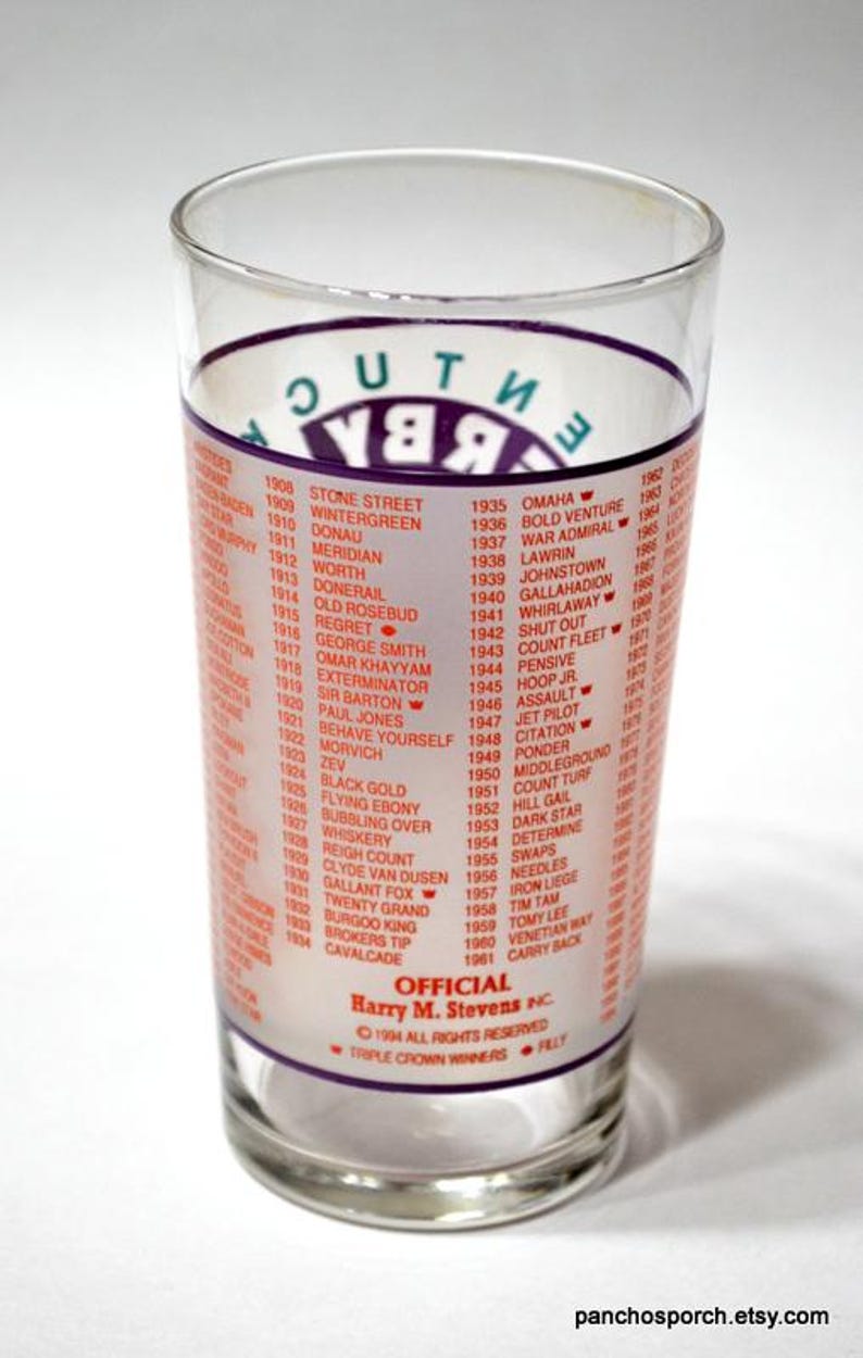 Puede incluir: Vaso transparente con una lista de ganadores de la Triple Corona de 1908 a 1961. El texto es rojo y blanco, con "Kentucky Derby" en morado. El vaso es cil&iacute;ndrico.