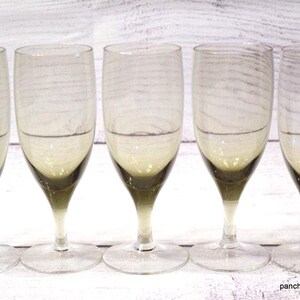 May include: A set of five clear glass goblets featuring a distinct ombre effect with a dark charcoal gray base that fades into a transparent upper bowl. Each glass has a slender stem and a circular foot, showcasing a smooth, minimalist design.