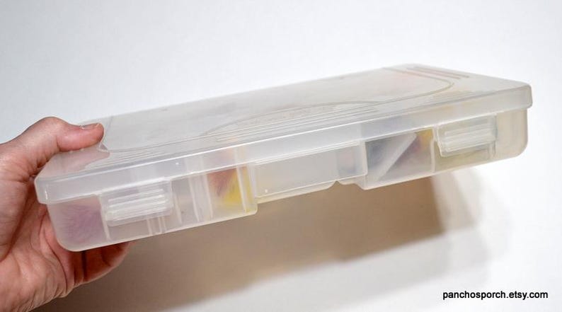 May include: A clear plastic storage box with a hinged lid and multiple compartments. The box is held in a hand and appears to contain small items. The box is rectangular and has a translucent appearance. The website address "panchosporch.etsy.com" is visible.