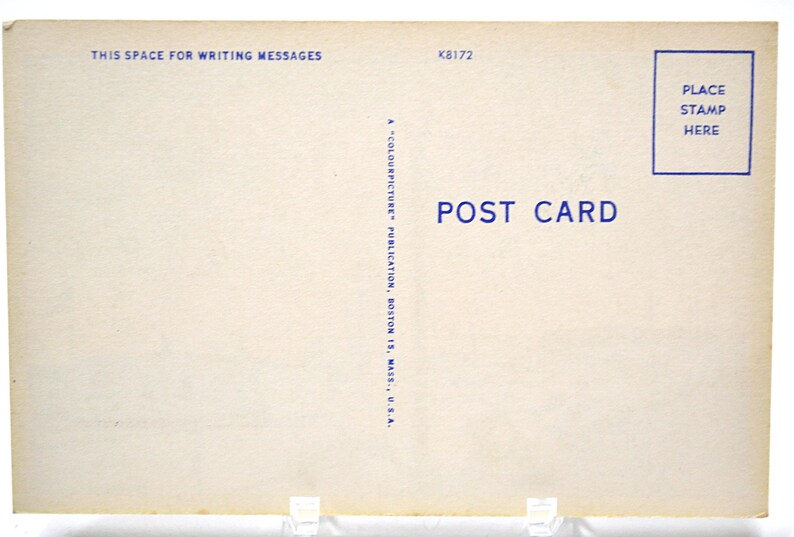 Op de afbeelding: Een vintage ansichtkaart met een cr&egrave;mekleurige achtergrond. De tekst "THIS SPACE FOR WRITING MESSAGES" staat bovenaan, en "POST CARD" is in het blauw gedrukt. Een blauw vak voor een postzegel staat in de rechterbovenhoek. De ansichtkaart wordt ondersteund door transparante plastic steunen.