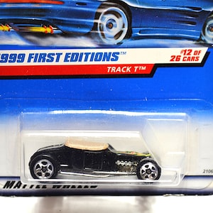 May include: A black 1999 First Editions Track T™ die-cast toy car, #12 of 26 cars, in its original packaging. The car has a tan convertible top and silver wheels. The packaging is blue with red and white text.