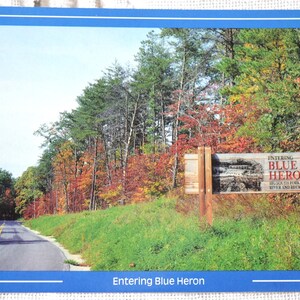 May include: A postcard with a photo of a road leading into a forest with fall foliage. A sign reads "Entering Blue Heron Big South Fork National River and Recreation Area".