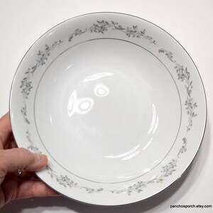 May include: A white ceramic bowl with a silver rim and a delicate floral design in shades of blue and gray.