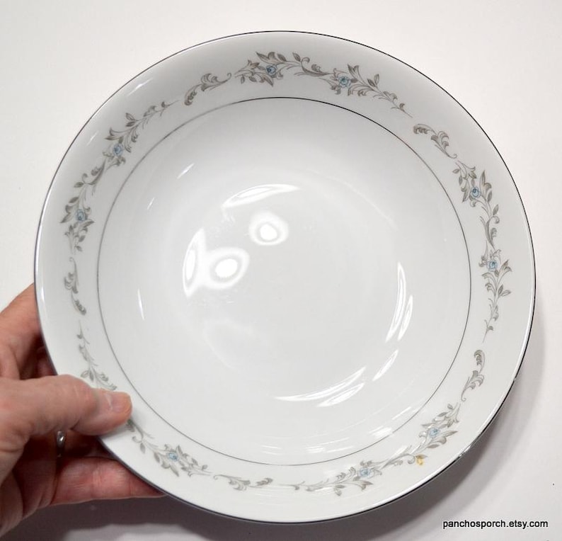 May include: A white ceramic bowl with a silver rim and a delicate floral design in shades of blue and gray.