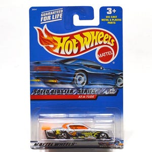 May include: A Hot Wheels die-cast toy car in a blue and orange package. The car is silver with orange and black accents. The package reads "Speed Blaster Series" and "Guaranteed for Life."