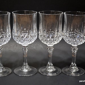 May include: Four clear crystal wine glasses with diamond-cut patterns on the bowls and decorative stems. The glasses have a classic design, with a rounded bowl and a slender stem, perfect for serving wine.