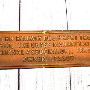 May include: A rectangular, bronze-coloured metal plaque with the text "SOUTHERN RAILWAY EQUIPMENT TRUST NO.4 OF 1970; THE CHASE MANHATTAN BANK (NATIONAL ASSOCIATION), TRUSTEE, OWNER, LESSOR." The plaque has two holes for mounting.