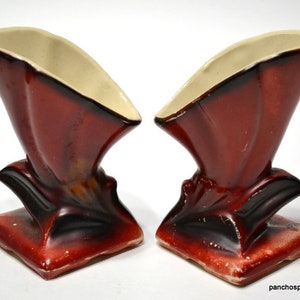 May include: Pair of vintage ceramic vases. Each vase has a square base and a flared, fan-shaped top. The exterior is a deep reddish-brown with black accents, and the interior is a cream color. The vases are approximately 6 inches tall.