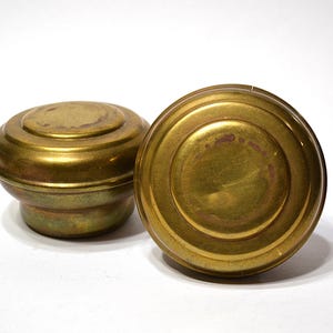May include: Two antique brass knobs with a warm, golden hue. The knobs have a rounded, tiered design with a slightly aged appearance. The surface shows subtle wear, adding to their vintage charm. Perfect for restoration projects.