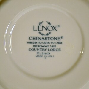 May include: Cream-colored Lenox Chinastone Country Lodge plate. The center features the Lenox logo, Chinastone, and product details. The plate is microwave safe and freezer to oven to table. Made in the USA.
