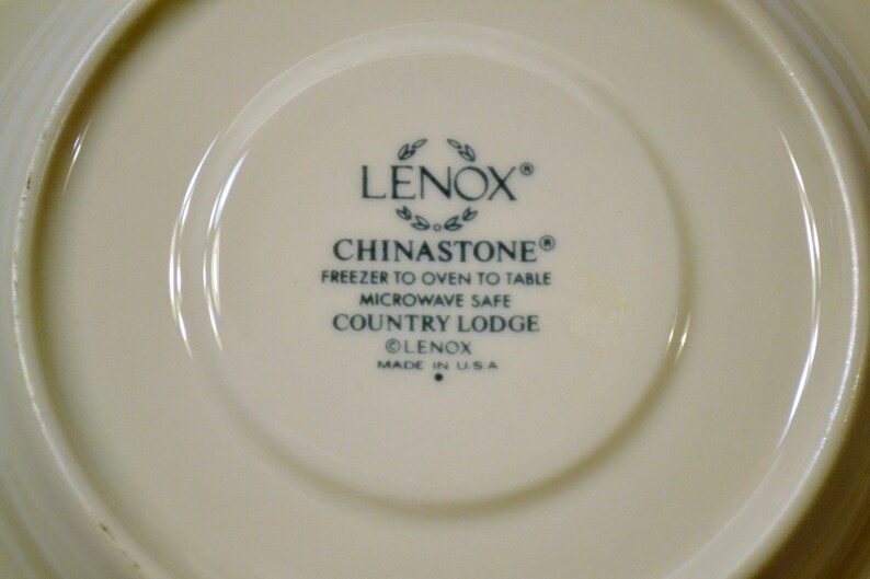 May include: Cream-colored Lenox Chinastone Country Lodge plate. The center features the Lenox logo, Chinastone, and product details. The plate is microwave safe and freezer to oven to table. Made in the USA.