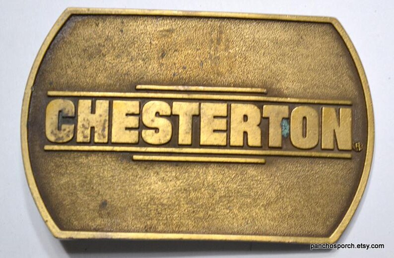 May include: A vintage brass belt buckle with the name "CHESTERTON" in raised letters. The buckle has a rectangular shape with rounded edges and a tarnished, aged appearance. The text is centered on the buckle.
