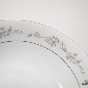May include: A white ceramic bowl with a silver rim and a delicate floral design in shades of gray and blue.