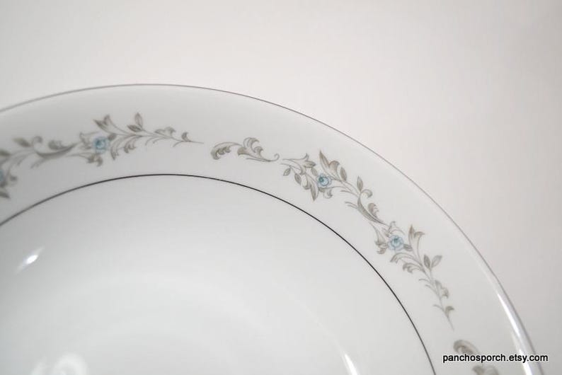 May include: A white ceramic bowl with a silver rim and a delicate floral design in shades of gray and blue.