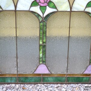 Op de afbeelding: Een glas-in-loodraam met een geometrisch ontwerp met roze rozen, groene bladeren en heldere en matte glaspanelen.