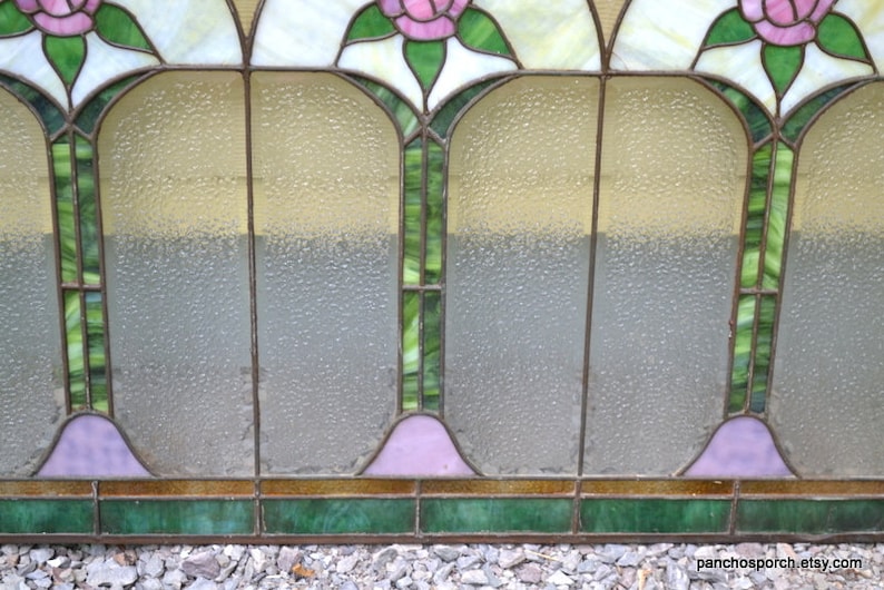Op de afbeelding: Een glas-in-loodraam met een geometrisch ontwerp met roze rozen, groene bladeren en heldere en matte glaspanelen.