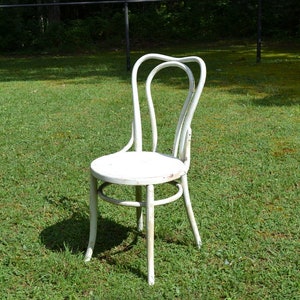 May include: White metal chair with a curved back and a round seat. The chair is sitting on a grassy lawn.