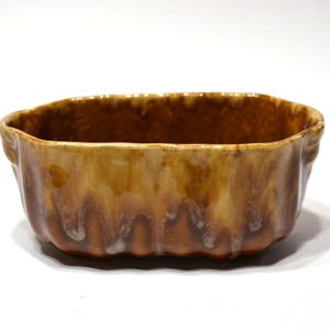 May include: An oval ceramic bowl featuring a glossy, multi-toned brown glaze with a vertical drip pattern. The exterior has a scalloped, fluted texture along the sides, and the rim is uneven, following the wavy contour of the bowl's structure.