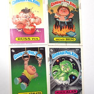 May include: Four rectangular Garbage Pail Kids trading cards featuring colorful illustrations. The cards are titled Russ Pus, Brewin' Bruno, Busted Armand, and Alien Alan, each displaying a unique character graphic with text labels and numbers.