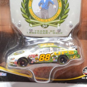 May include: A die-cast model of a NASCAR race car, featuring the number 88 and UPS branding. The packaging includes text that reads "Tribute to a Legend" and "50 Years of Legendary Golf."