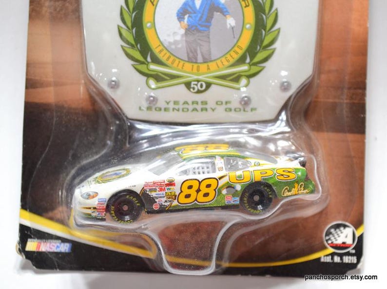 May include: A die-cast model of a NASCAR race car, featuring the number 88 and UPS branding. The packaging includes text that reads "Tribute to a Legend" and "50 Years of Legendary Golf."