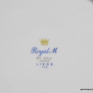 May include: A white porcelain plate with a gold crown and blue text that reads "Royal M by Saji Japan Liege 713".