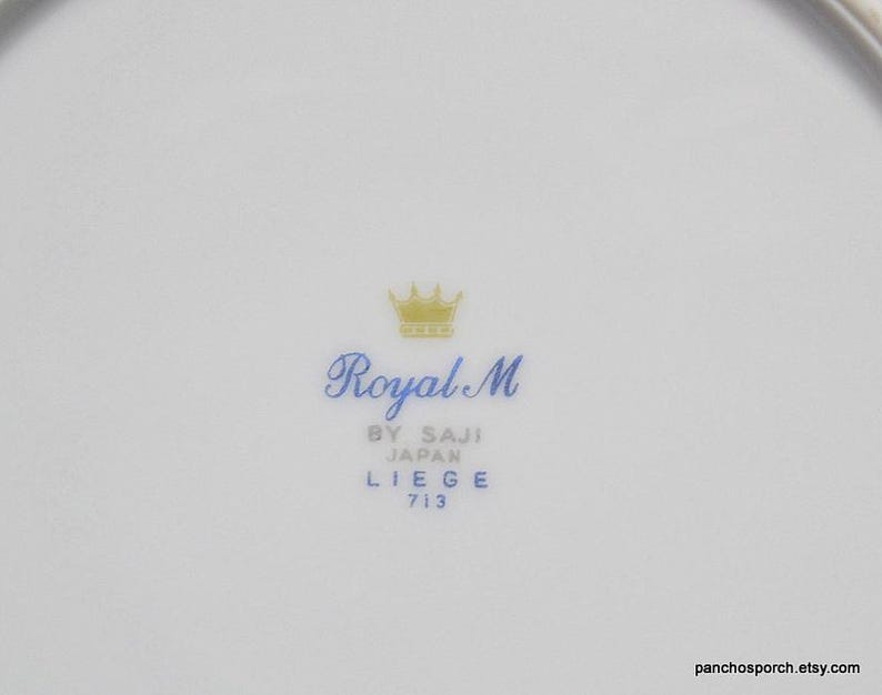 May include: A white porcelain plate with a gold crown and blue text that reads "Royal M by Saji Japan Liege 713".