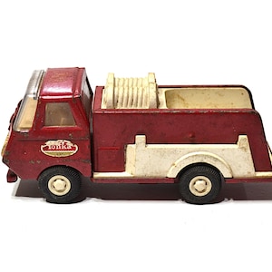 May include: Vintage Tonka fire truck toy in red and cream colors. The toy truck features black wheels, a ladder reel, and the Tonka logo on the side. A classic collectible toy.