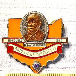 May include: A vintage Ohio Lions District 13 pin with a portrait of Benjamin Harrison, the text "HONOLULU 1983", and the organization's name. The pin is shaped like Ohio, with orange and red enamel.