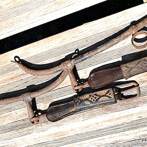 May include: Two antique metal horse bits with leather straps. The bits are rusty and have a worn look. The straps are brown leather with decorative stitching.