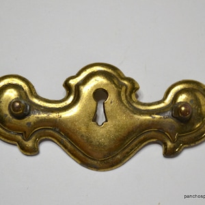 May include: A brass drawer pull with a keyhole design. The pull has a decorative, ornate shape with two rounded ends.