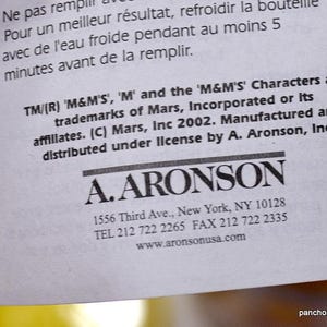 May include: A close-up of a white paper with text in English and French. The text includes trademark information for 'M&M'S' characters and the A. Aronson company's contact details, including an address in New York.