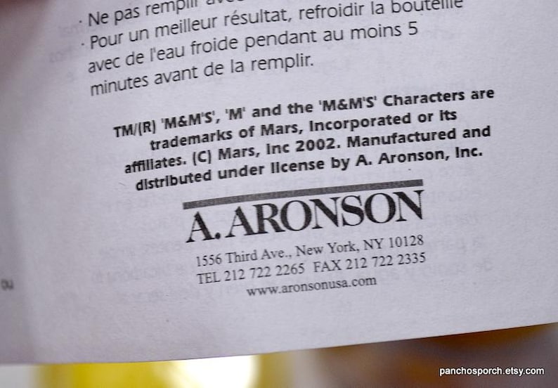 May include: A close-up of a white paper with text in English and French. The text includes trademark information for 'M&M'S' characters and the A. Aronson company's contact details, including an address in New York.