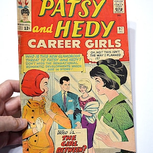 May include: A retro comic book cover for "Patsy and Hedy Career Girls". The cover is predominantly red, with illustrations of characters and speech bubbles. Text includes "Who is the Girl Between?" and "Marvel Comics".