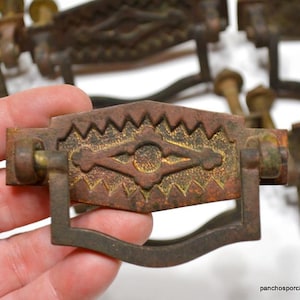 May include: Set of eight antique brass drawer pulls with a geometric design. The pulls have a diamond shape in the centre with a textured surface and a curved, arched handle.