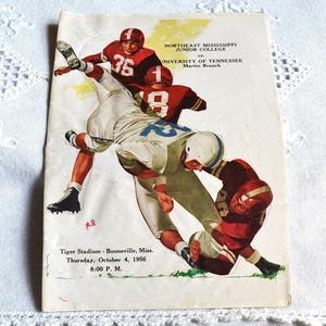 May include: Vintage football game program featuring a dynamic illustration of players in action. The program cover displays the text "Northeast Mississippi Junior College vs. University of Tennessee, Martin Branch." The game was held at Tiger Stadium in Booneville, Mississippi, on October 4, 1956.